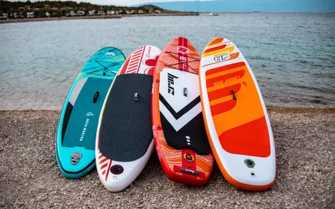 Cztery kolorowe deski SUP dla dzieci stoją na plaży, gotowe na wodne przygody.