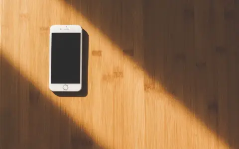 Biały smartfon leży na drewnianym blacie. Słońce rzuca cień. Jak namierzyć telefon, gdy zaginie?