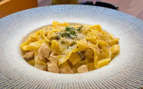 Pyszny makaron włoski z kawałkami kurczaka w kremowym sosie, posypany ziołami i parmezanem.