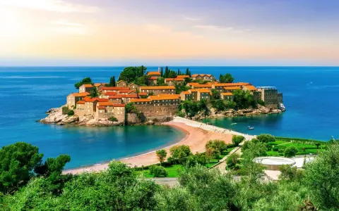 Drömresa till Montenegro: en pittoresk ö med stenhus och röda tak, omgiven av turkost hav. Perfekt för en solsemester.