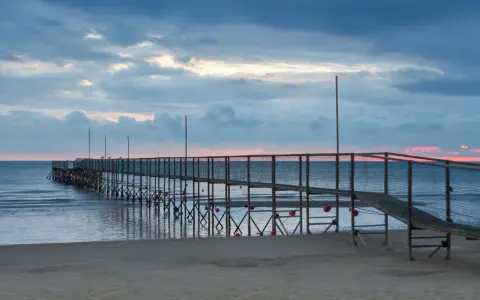 Molo di Rimini Rivazzurra al tramonto, con cielo nuvoloso e mare calmo.