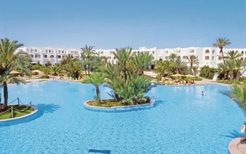 Słoneczny basen w Djerba Resort (dawniej Vincci) otoczony palmami i białymi budynkami.