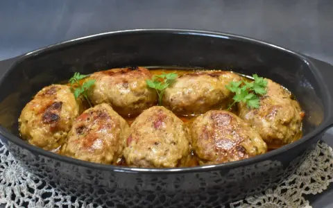 Pyszne roladki z mięsa mielonego z piekarnika, polane sosem i udekorowane natką pietruszki, prezentują się apetycznie w czarnej brytfannie.