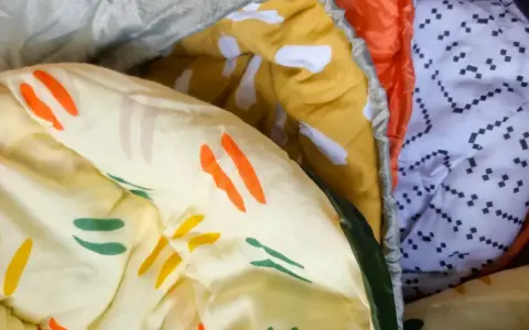 Bunte Muster auf einem Schlafsack aus Baumwolle oder Polyester. Ein gelber Stoff mit orangen und grünen Streifen, daneben ein orangefarbener und ein weißer Stoff mit schwarzen Punkten.