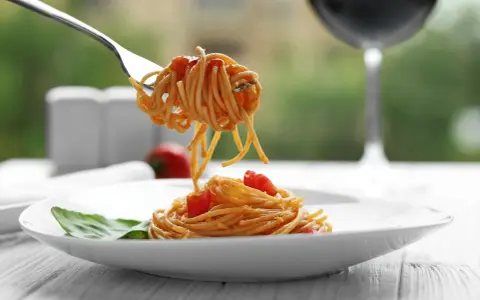 Widok na talerz spaghetti z sosem pomidorowym i listkiem bazylii. Widelec podnosi porcję makaronu. Idealne pytanie: jakie wino do bolognese?