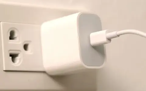 Biała ładowarka z kablem podłączona do gniazdka elektrycznego. Typ wtyczki EU.