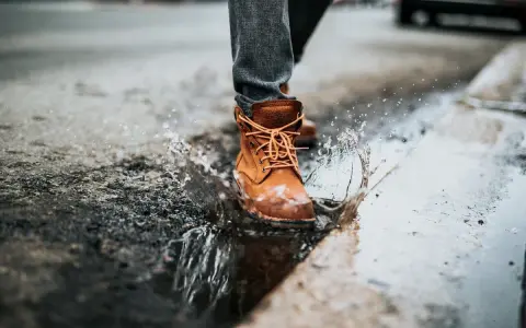 Botas de cuero marrón salpican un charco, demostrando que el cuero es impermeable.