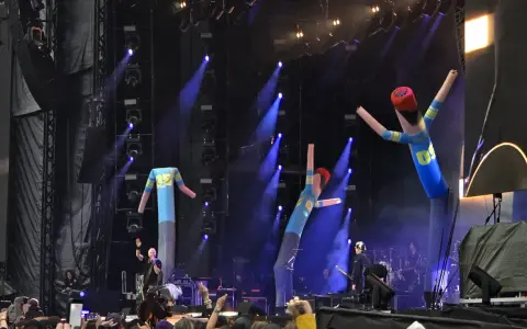 The Offspring Sverige spelar live med uppblåsbara figurer på scenen. Blå ljus och rök skapar en festlig stämning.