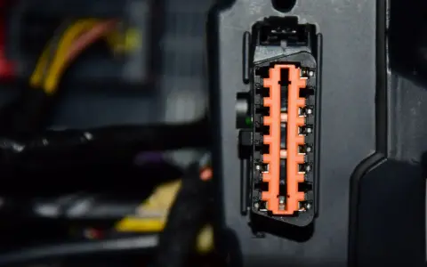 Pomarańczowe złącze elektryczne w samochodzie Mercedes B180, otoczone przewodami.