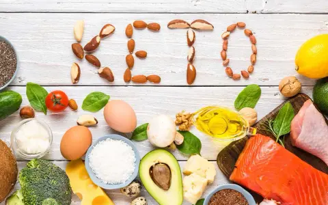 Słowa "KETO" ułożone z orzechów i nasion. Wokół składniki diety keto: ryba, mięso, jajka, awokado, olej, ser, warzywa.