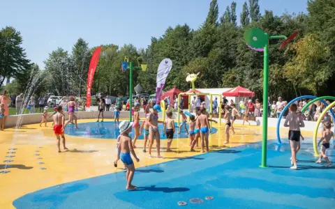Dzieci bawią się na wodnym placu zabaw, jednej z atrakcji dla dzieci w Katowicach. Woda tryska z kolorowych elementów, tworząc radosną atmosferę.