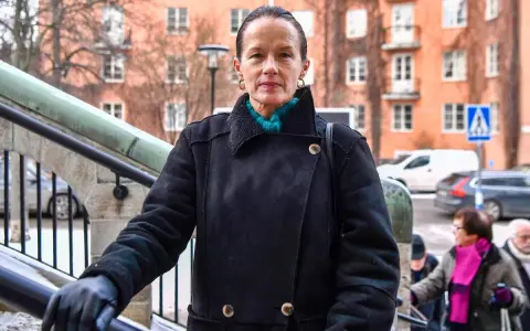 Malin Berghagen, trots att hon verkar sjuk, går uppför en trappa i en svart kappa.