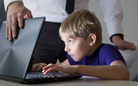 Chłopiec pochłonięty grą na laptopie, a dorosły próbuje pomóc w leczeniu uzależnienia od komputera.