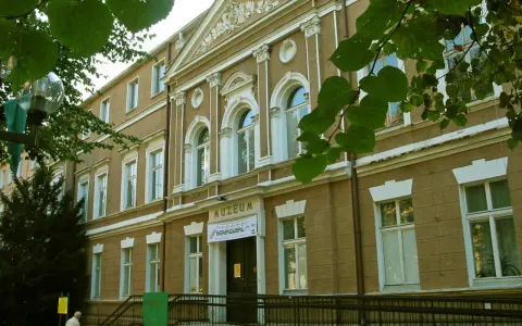 Fasada muzeum w Zielonej Górze, z napisem "MUZEUM". W pobliżu drzewa i ławka.