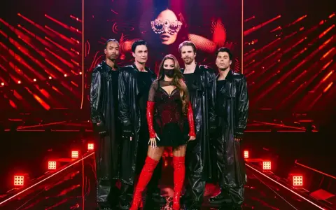 Eurovision svenska kommentatorer: artist med dansare i glänsande svarta rockar och rött, på en scen med röda ljus.