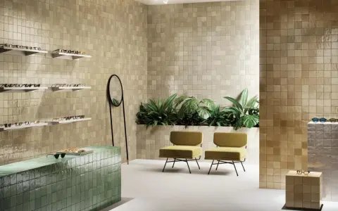 Un espace moderne avec des murs recouverts de **zellige** beige, un comptoir vert émeraude, des plantes luxuriantes et des chaises jaunes.