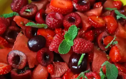 Macedonia di frutta fresca e colorata: fragole, ciliegie, lamponi e anguria, guarnita con foglie di menta.