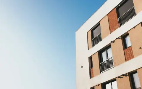 Façade d'un immeuble moderne avec balcons et volets roulants, idéal pour mettre son appartement en location. Ciel bleu clair.