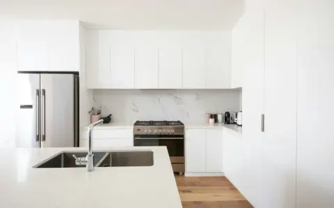 Cocinas blancas elegantes con encimeras de cuarzo, electrodomésticos de acero inoxidable y suelo de madera.