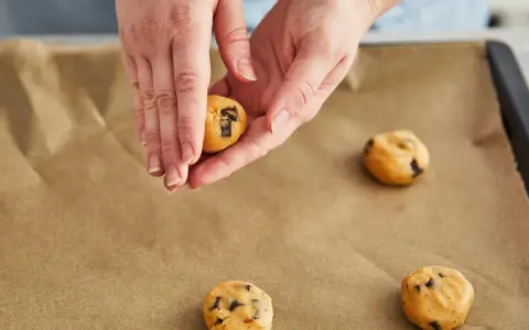 Hände formen Teig für einen Skillet Cookie mit Schokoladenstückchen auf Backpapier.