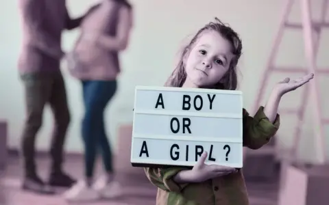 Dziewczynka trzyma tabliczkę "A BOY OR A GIRL?". Rodzice czekają na dziecko, a płeć można poznać do 20. tygodnia ciąży.
