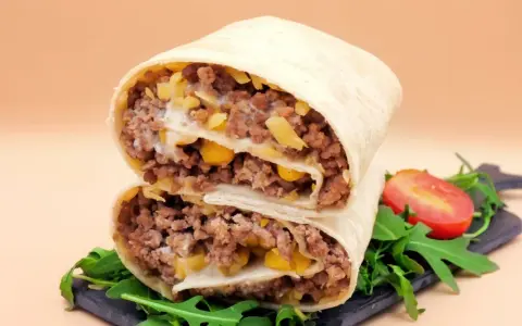 Pyszna tortilla z mięsem mielonym, kukurydzą i serem, przekrojona na pół, z rukolą i pomidorkiem.