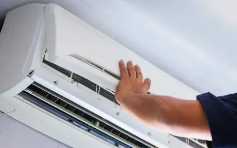 Ręka technika otwiera obudowę klimatyzatora do sprawdzenia szczelności.
