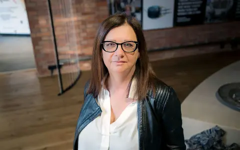 Małgorzata Szczęśniak w okularach i czarnej ramonesce, zamyślona.