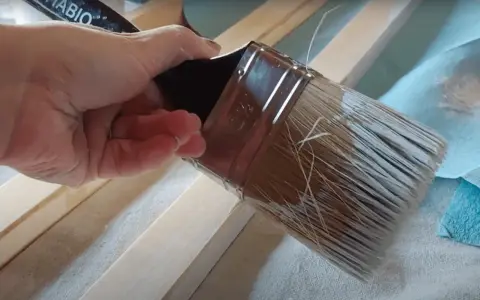 Mano aplica pintura con un pincel seco sobre listones de madera.