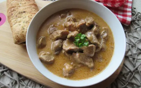 Aromaticzny gulasz wieprzowy w kremowym sosie, udekorowany natką pietruszki, podany z chrupiącym pieczywem.