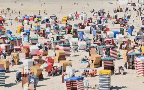 Bunte Strandkörbe säumen den Sandstrand, einige Menschen entspannen sich, andere spielen Volleyball. Ein typischer fkk strand.