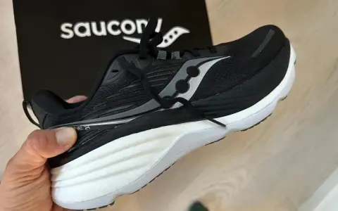 En svart Saucony löparsko, modell Guide 24, hålls upp. Denna sko är designad för att ge stöd och stabilitet, vilket är viktigt för att förstå vad pronation betyder för löpare.