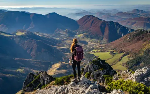 Widok na jesienne pasmo górskie Mała Fatra. Kobieta z plecakiem podziwia panoramę z kamienistego szczytu.