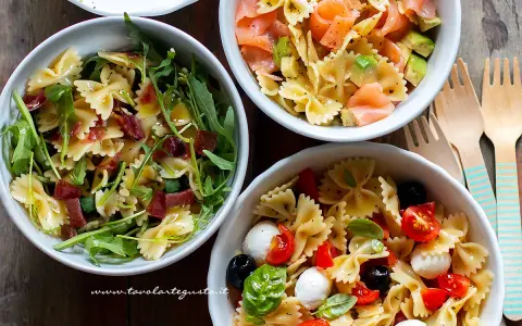 Tre ciotole di pasta fredda saporita: una con salmone e avocado, una con rucola e prosciutto, e una con pomodorini, mozzarelline e olive.