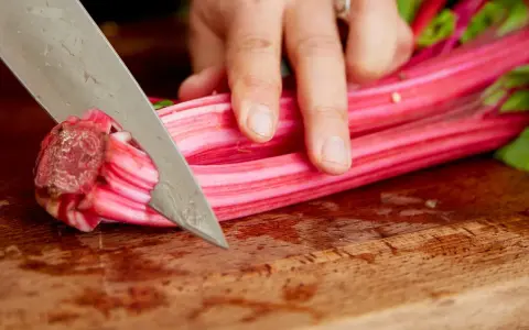 Eine Hand schneidet mit einem Messer die roten Stiele von Mangold, um ihn zuzubereiten.