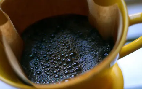 Heißer Kaffee mit Schaum in einer gelben Tasse. Ein Muntermacher, der den Unterschied zwischen Teein und Koffein verdeutlicht.