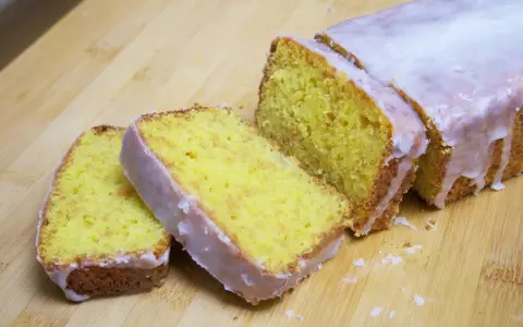 Un delicioso pastel de limón, cubierto con glaseado blanco, cortado en rebanadas sobre una tabla de madera.