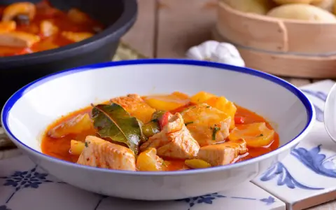 Bol de patatas con bonito en salsa roja, decorado con hojas de laurel.