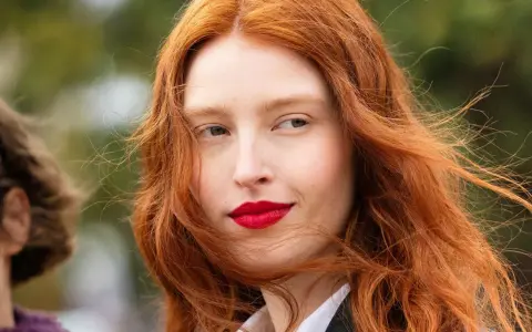 Eine Frau mit leuchtend roter haarfärbung und roten Lippen, ihr Haar weht im Wind.
