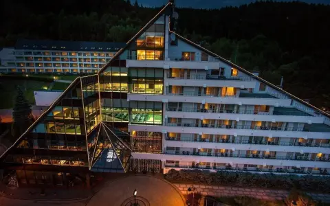 Nowoczesny hotel Klimczok Resort & Spa nocą, z oświetlonymi oknami i wejściem. Wiele pozytywnych hotel klimczok resort & spa opinie potwierdza jego urok.