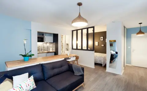 Aménagement studio 30m2 : salon cosy, cuisine moderne, chambre séparée par verrière, et coin repas.