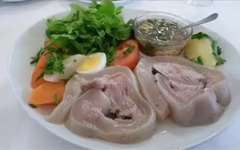 Une assiette de tête de veau gastronomique, accompagnée de légumes frais, d'un œuf dur, de carottes et d'une sauce savoureuse.
