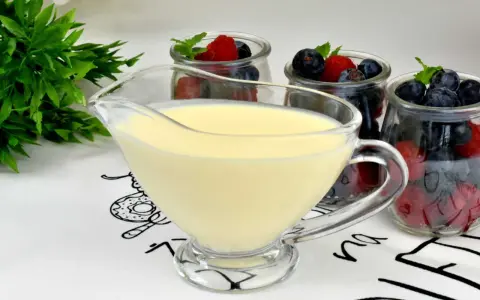 A glass boat filled with smooth, creamy krem angielski, ready to be poured over fresh berries in jars.