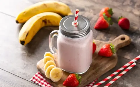 Un délicieux smoothie fraise banane dans un bocal en verre, garni de fruits frais et de pailles rayées.