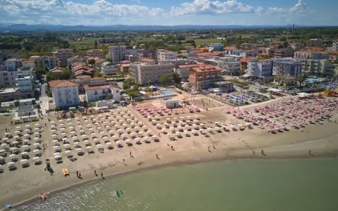 Vista aerea di una spiaggia affollata con ombrelloni rosa e bianchi, hotel e case nel centro storico di Torre Pedrera.