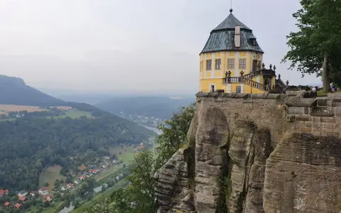 Żółty pałac na skale, część twierdzy Königstein, góruje nad doliną rzeki i lasami.