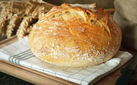 Ein knuspriges, schnelles Brot mit Backpulver, das auf einem karierten Tuch liegt. Im Hintergrund sind Ähren und ein Sack zu sehen.