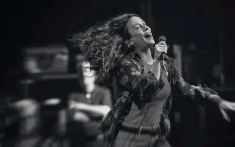 Energetyczny alanis morissette koncert, wokalistka śpiewa z pasją, włosy rozwiane w locie.