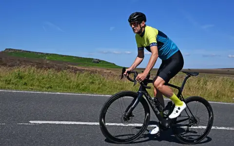 Man cycling on max speed on a scenic road with hills in the background.
