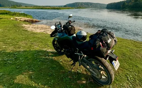 Motocykl z bagażem nad rzeką, gotowy do podróży po Litwie. Przepisy drogowe to podstawa bezpiecznej wyprawy.